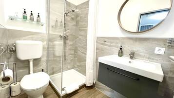 A modern bathroom with a glass-enclosed shower, a toilet, a sink with a mirror, and toiletries on a shelf.