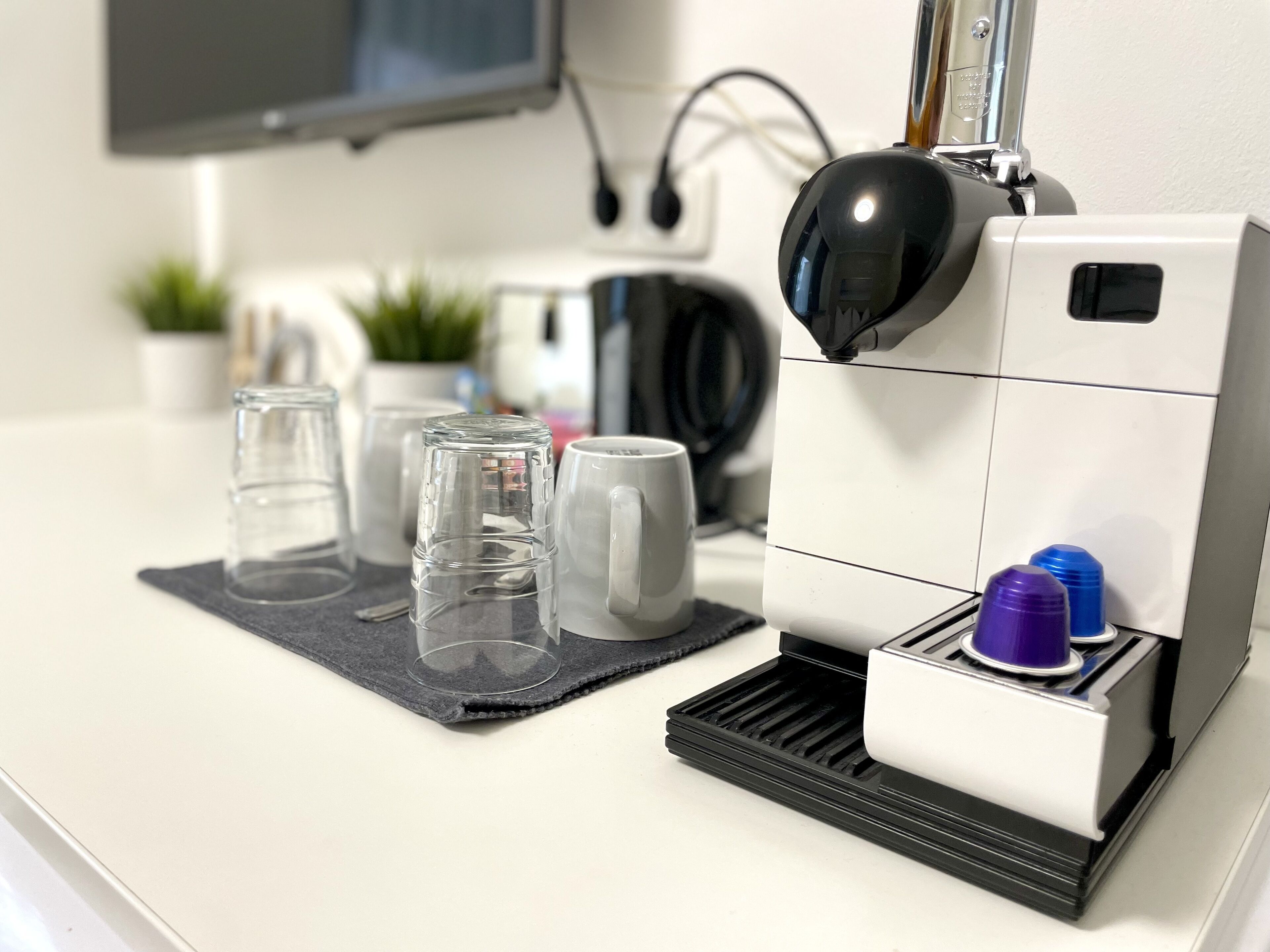 A coffee machine with a drip tray, a white mug, and a glass on a countertop.