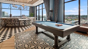 A pool table in a room with large windows, a bar area, and a patterned floor. - Cincinnati City Club Apartments by Airriva (Cincinnati)