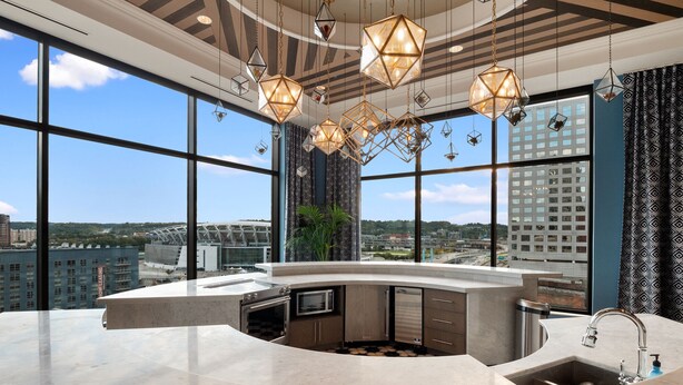 A modern kitchen with a large island, a built-in oven, and a sink. It features large windows offering a city view. - Cincinnati City Club Apartments by Airriva (Cincinnati)