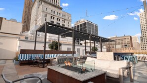 A rooftop terrace with a fire pit, seating area, and views of city buildings. - Cincinnati City Club Apartments by Airriva (Cincinnati)