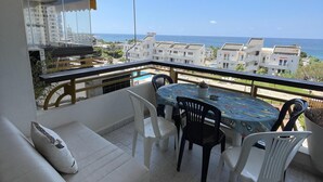 Een balkon met een eettafel en stoelen, een bank en uitzicht op zee en gebouwen.