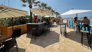 Een buitenterras met tafels, stoelen, parasols en een bar.