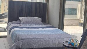 Ein modernes Schlafzimmer mit einem großen Bett, einer Couch und Blick auf Gebäude durch große Fenster.