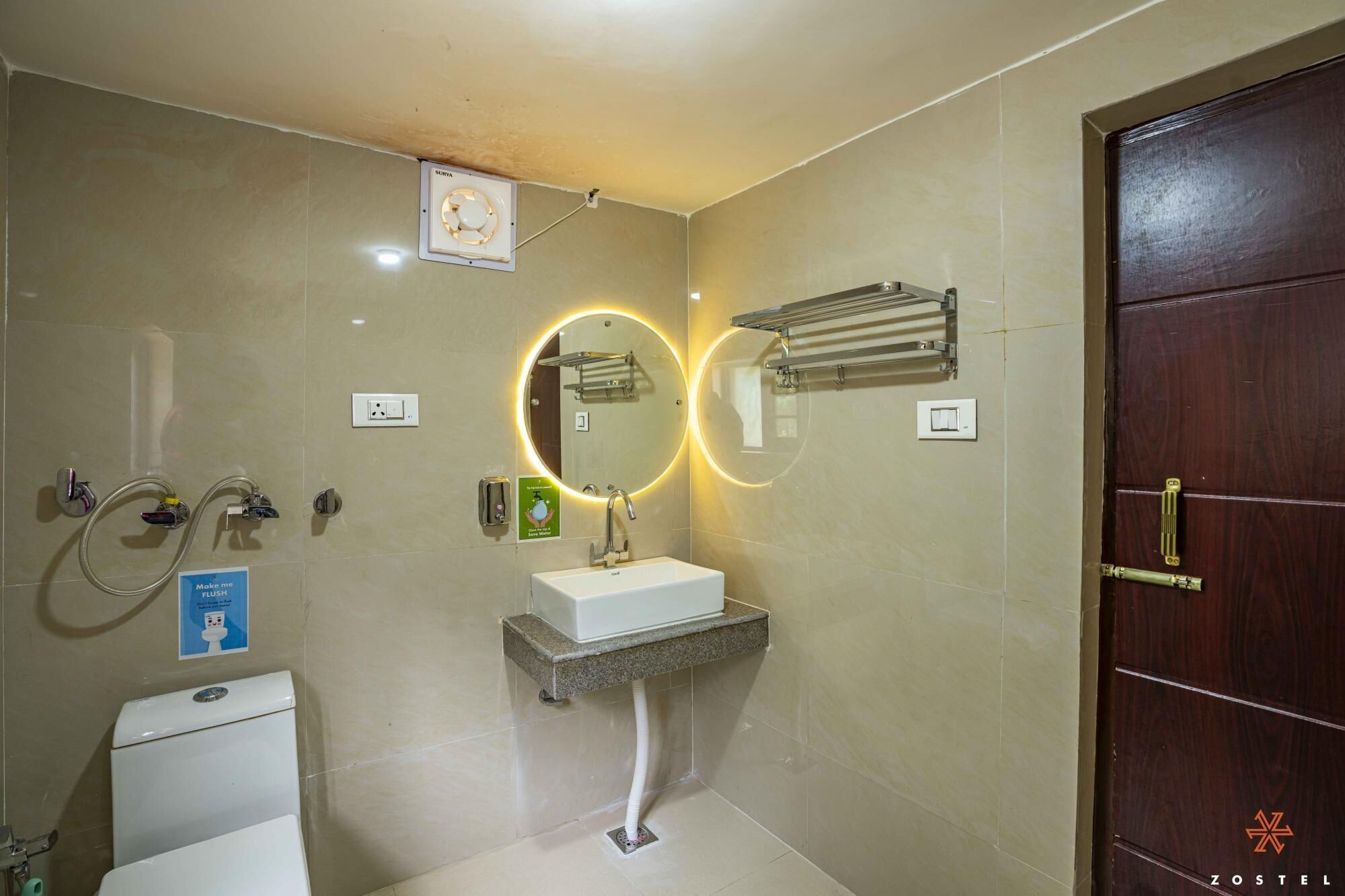 A bathroom with a toilet, sink, and shower. There are towel racks and a mirror with a circular light.