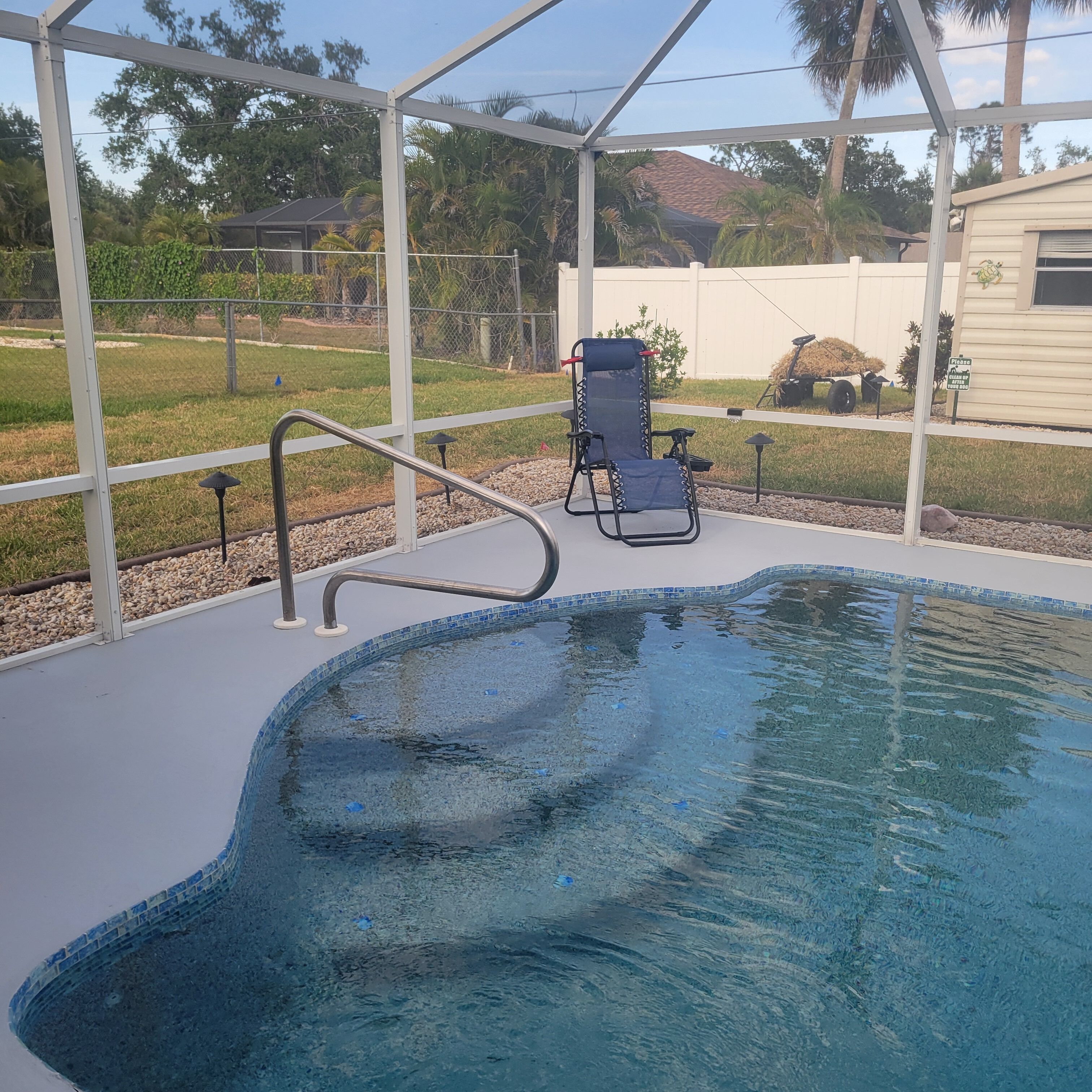 A pool area with a clear blue pool, a lounge chair, and a pergola structure.