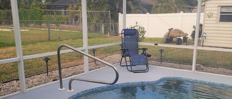 A pool area with a clear blue pool, a lounge chair, and a pergola structure.