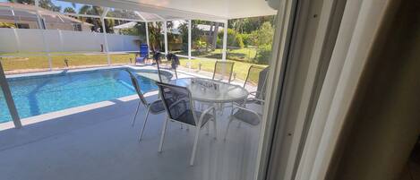 A covered outdoor area with a pool, chairs, and a table.