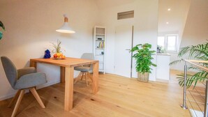 A modern, open-plan living space with a wooden dining table, two chairs, a hanging light fixture, a bookshelf, and a potted plant. - Moderne, Helle Wohnung (Heidelberg)