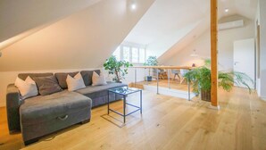 A loft-style living room with a sofa, a coffee table, and a dining area with a railing. - Moderne, Helle Wohnung (Heidelberg)