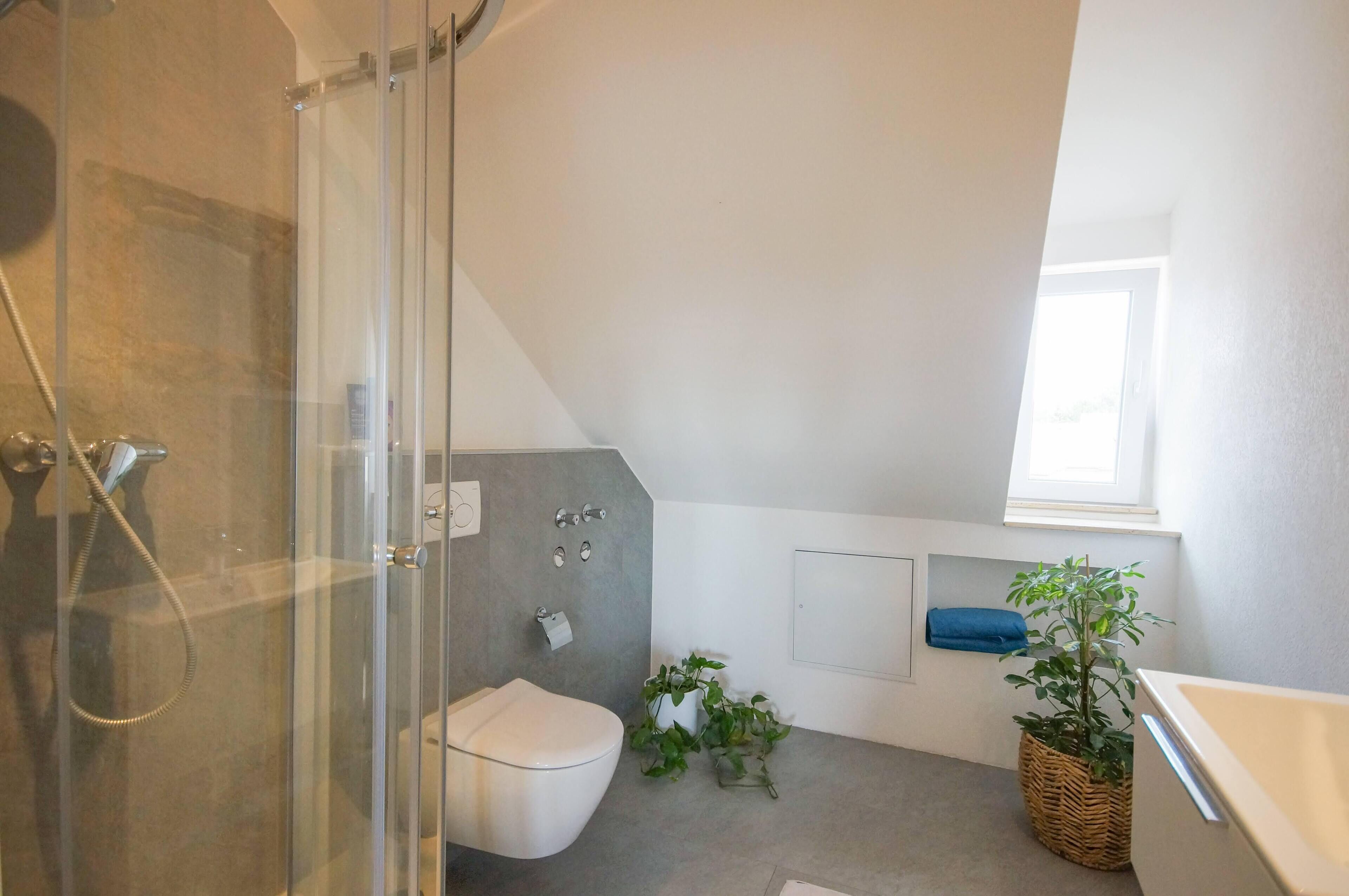 Un baño moderno con cabina de ducha de vidrio, inodoro, bañera y una ventana pequeña.