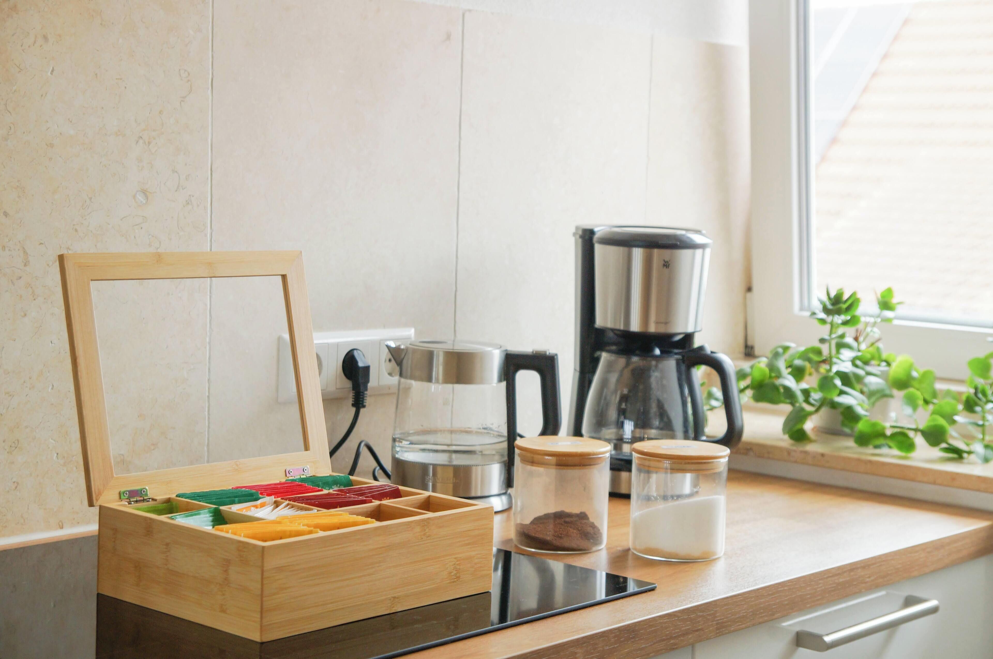 Eine Küche mit einer Holzkiste, Gläsern, einer Kaffeemaschine und einem Fenster mit Pflanzen.