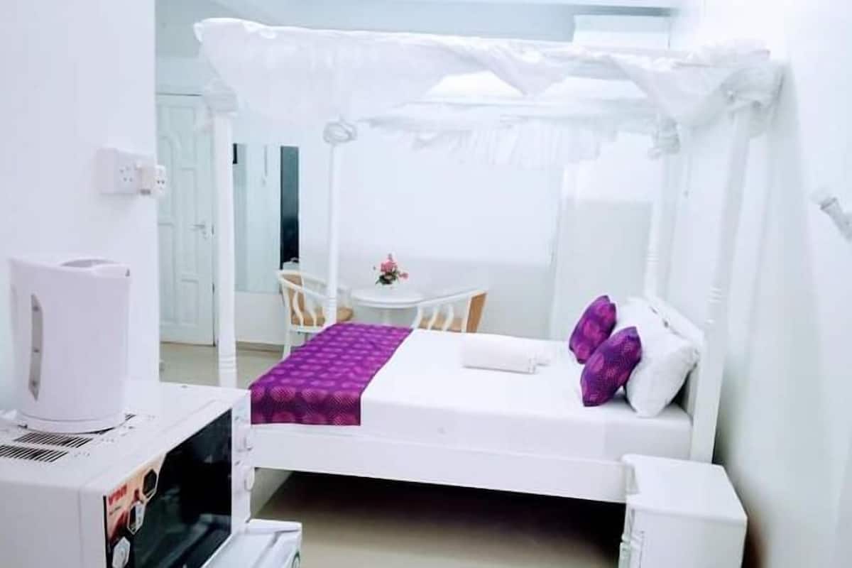 Una cama blanca con dosel, una pequeña mesa con sillas y una cafetera blanca.