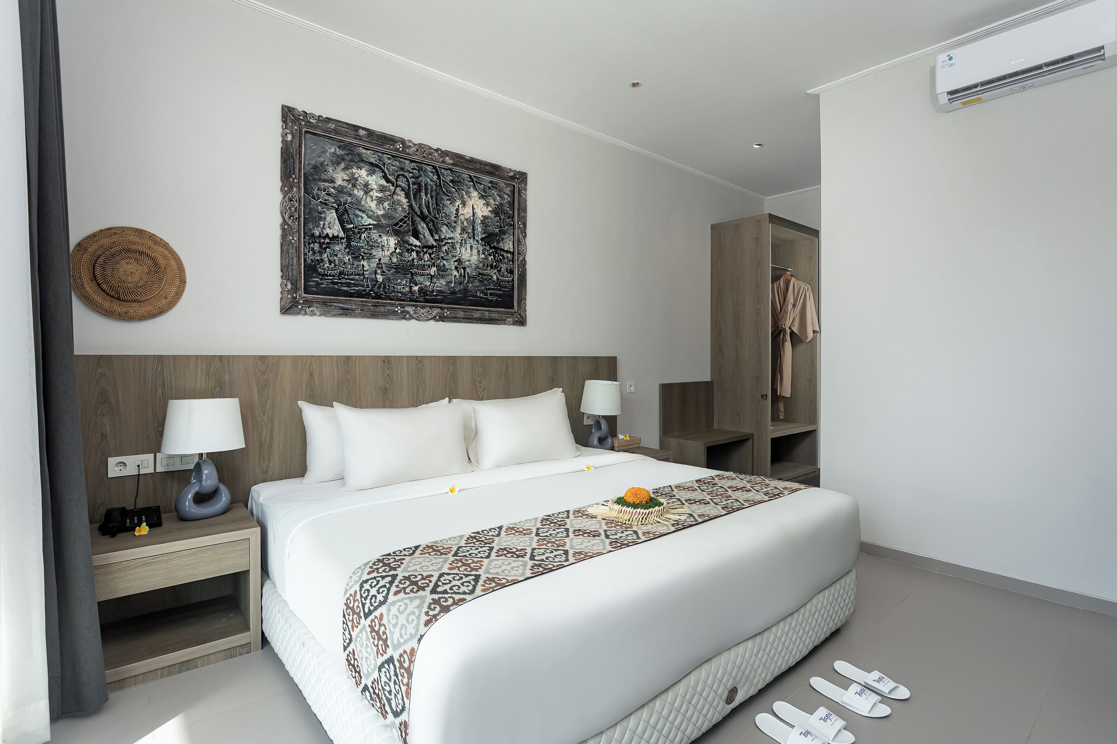Une chambre d’hôtel moderne avec un grand lit, une table de chevet avec une lampe, un climatiseur fixé au mur et une œuvre d’art encadrée au-dessus du lit.