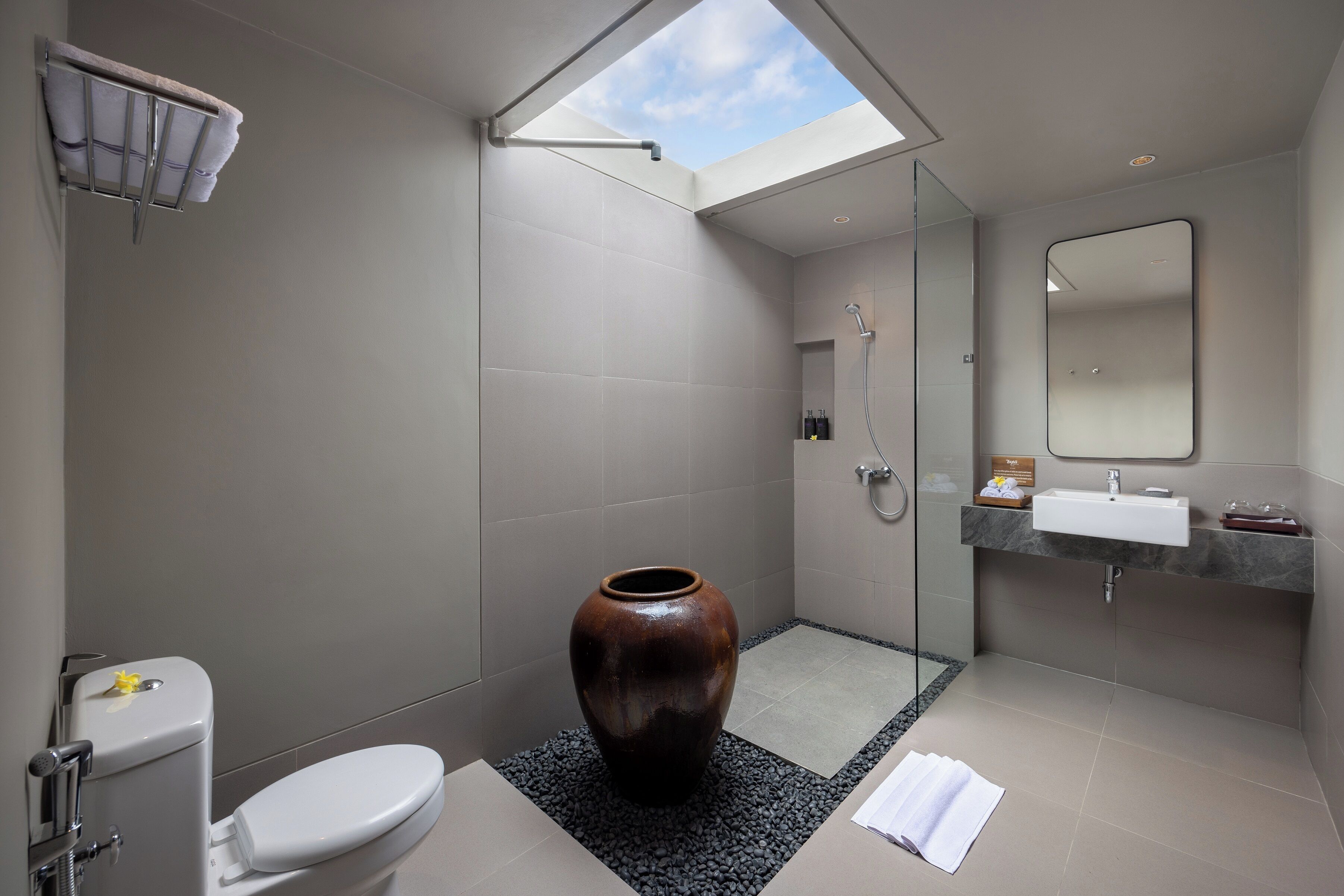A modern bathroom with a skylight, a large vase, a toilet, and a shower area.