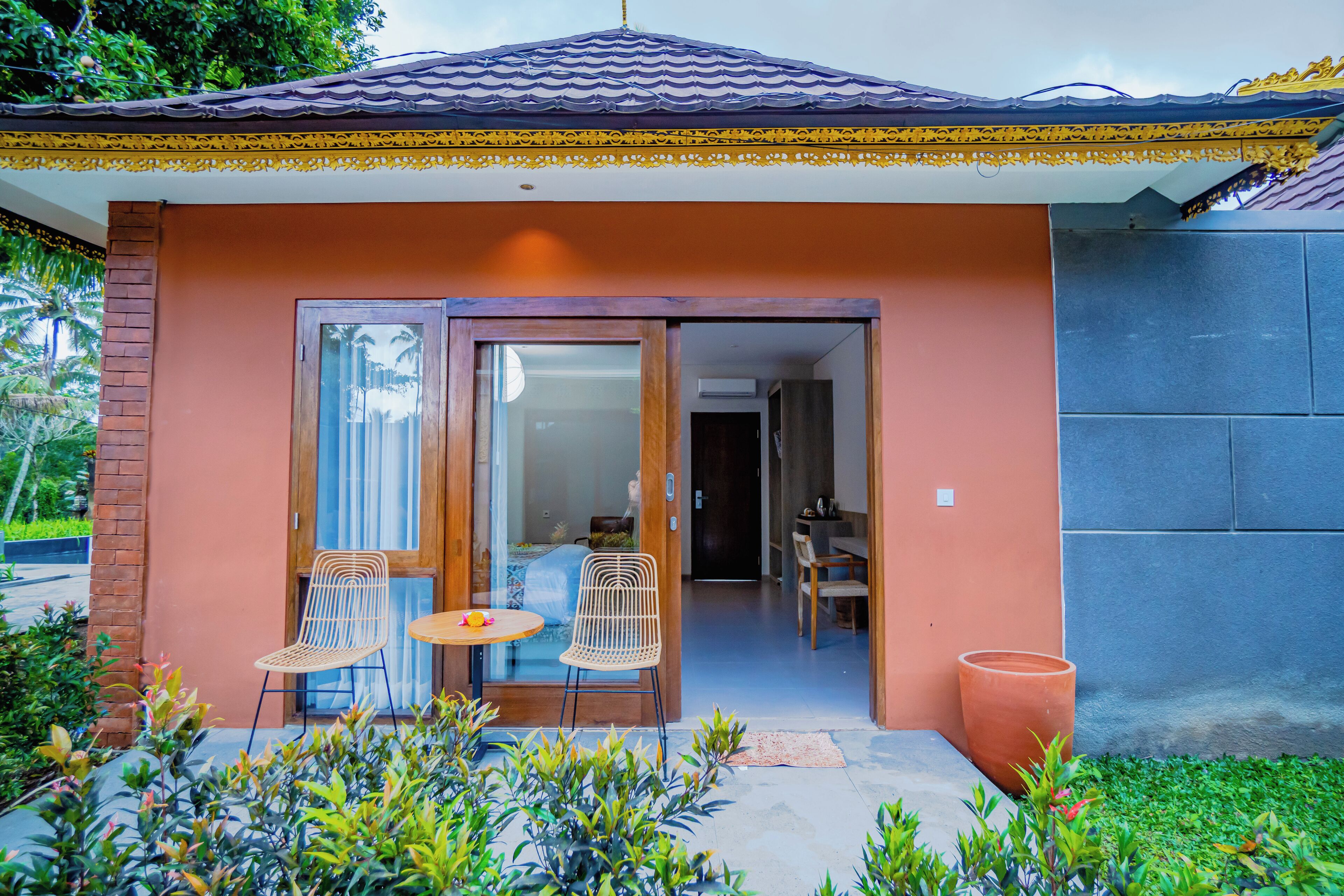 A house with a tiled roof, a wooden door, and a small patio with two wicker chairs and a table.