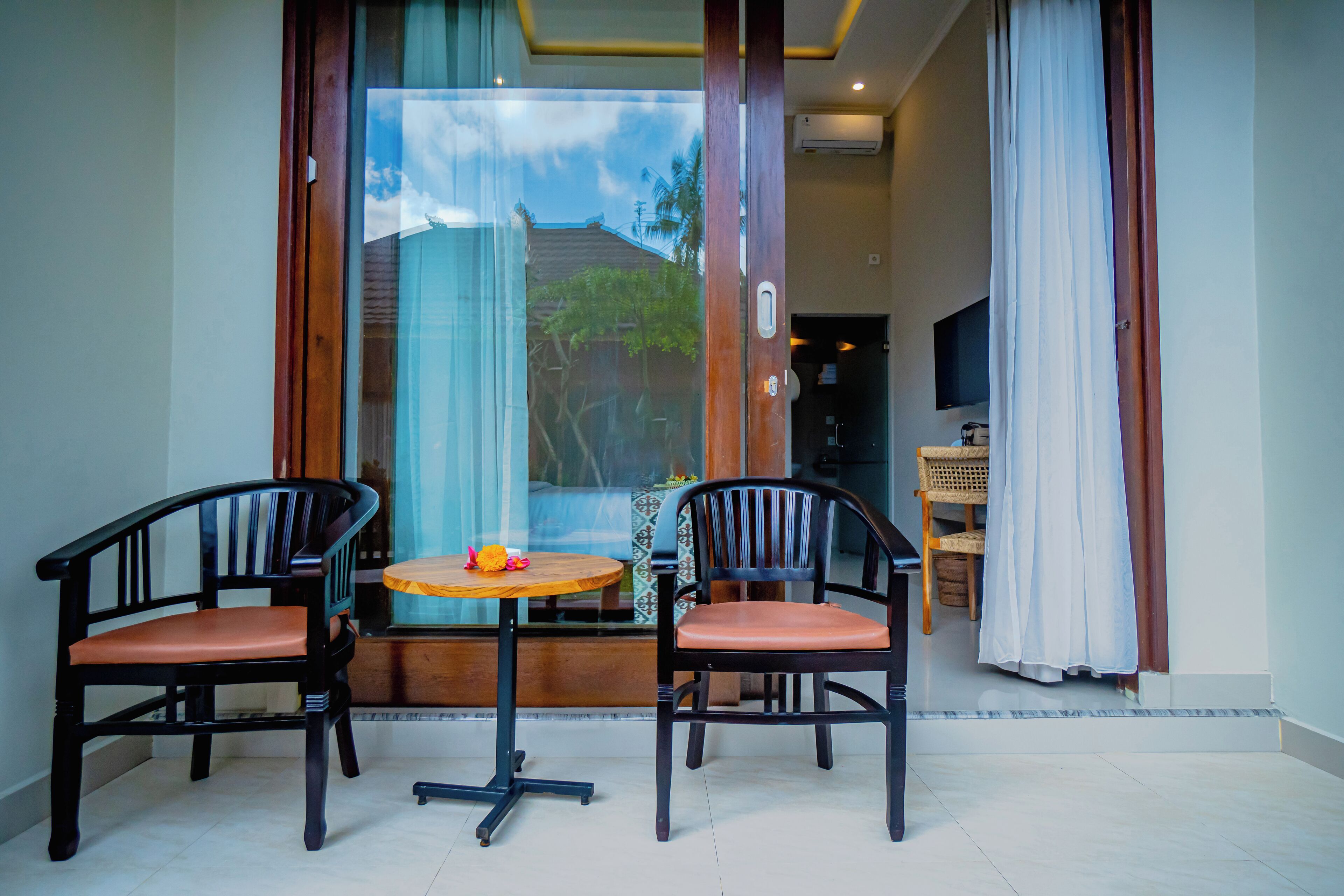 A room with two wooden chairs, a small round table, and a view through a glass door to the outside.