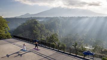 A person practicing yoga on a rooftop with a view of a mountain and forest.