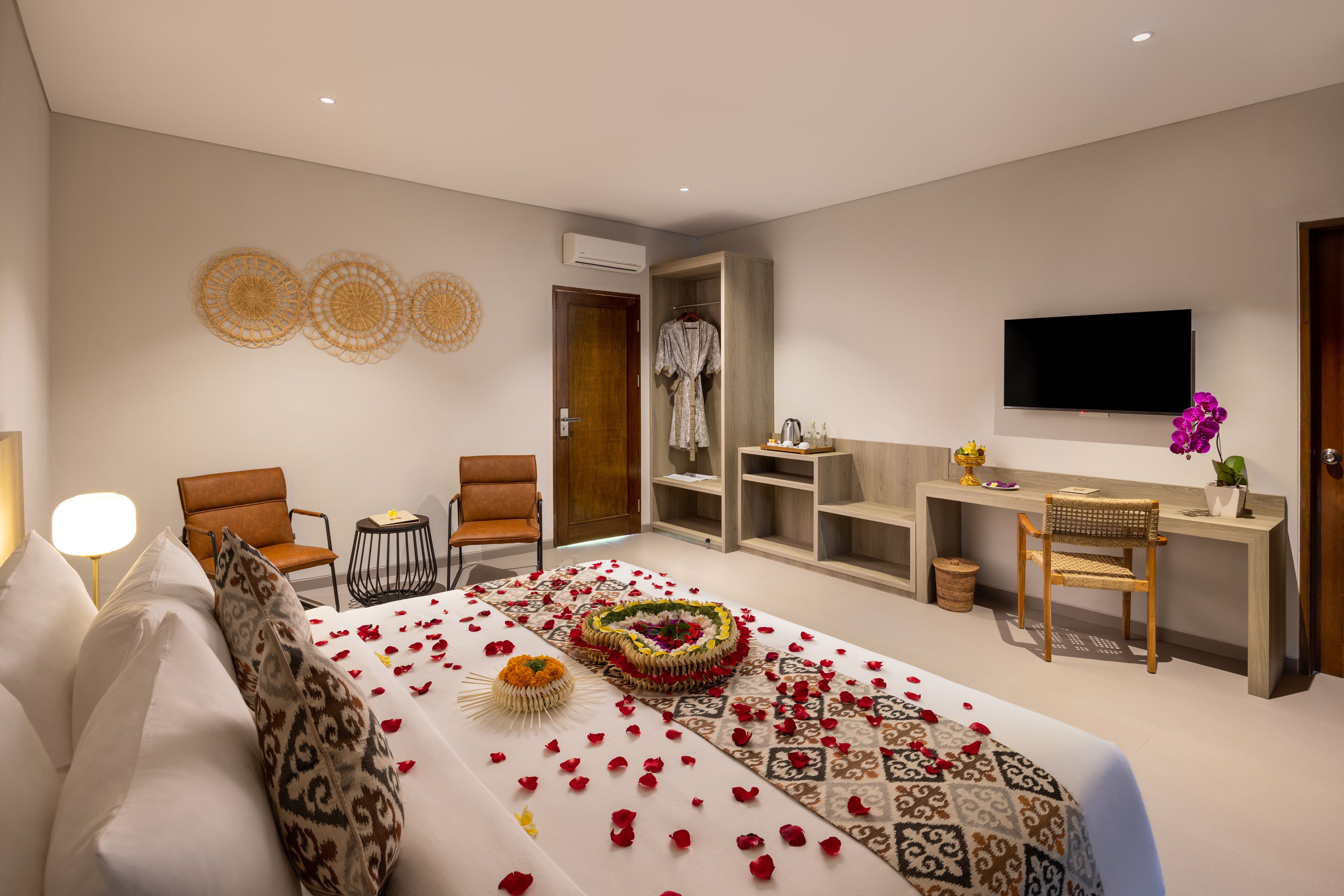 A hotel room with a large bed, two armchairs, a TV, and a small desk with a plant.