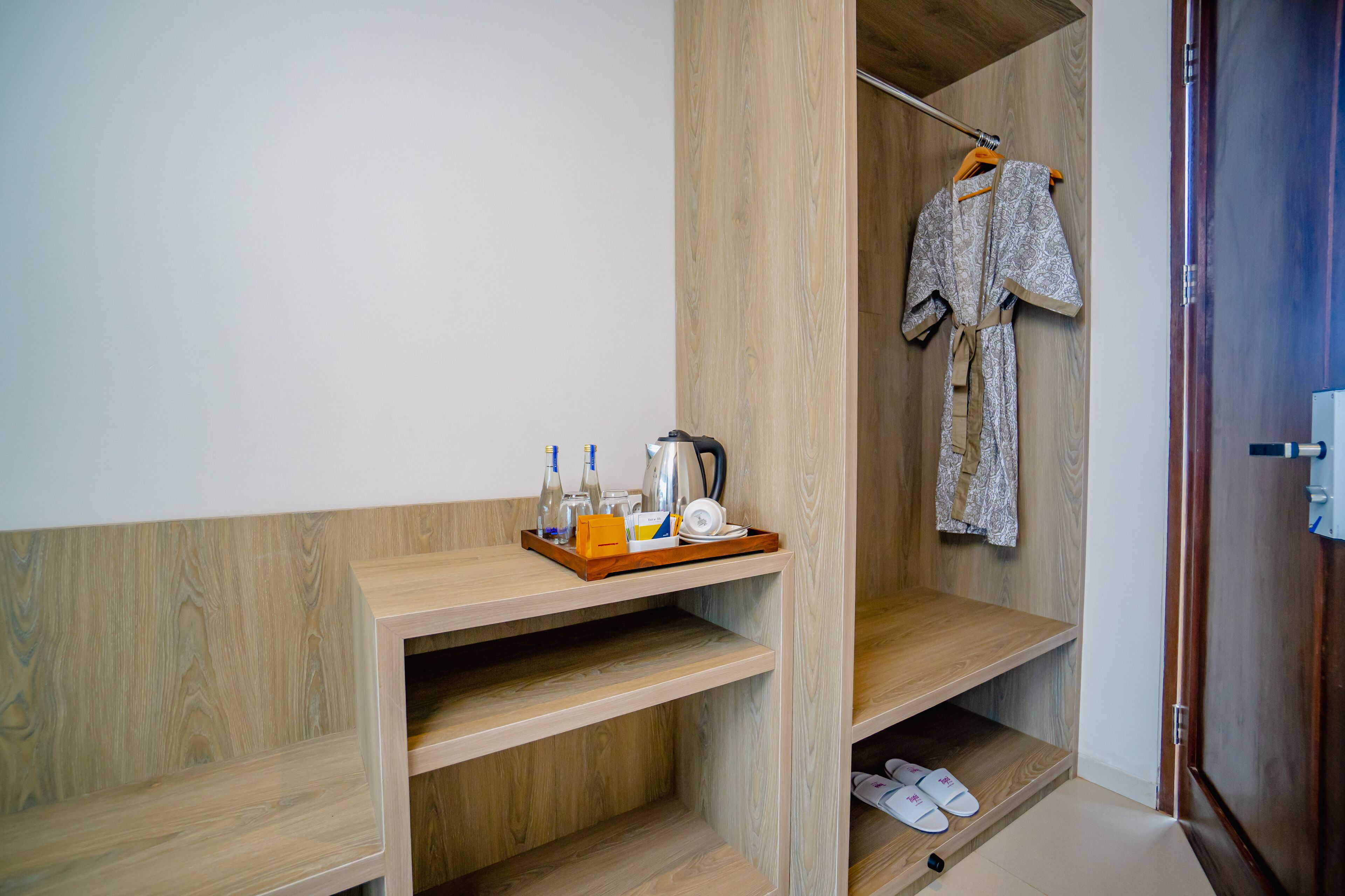 Una estantería de madera con una bandeja que sostiene botellas y una tetera, un par de pantuflas y una prenda colgando.