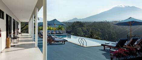 Un área de piscina en la azotea con sillones de descanso y sombrillas, con vistas a un paisaje montañoso.