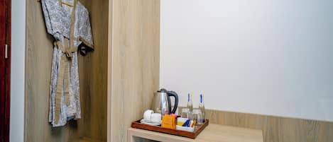 A hotel room with a wooden wardrobe, a hanging robe, and a tray with a kettle, cups, glasses, and bottles.