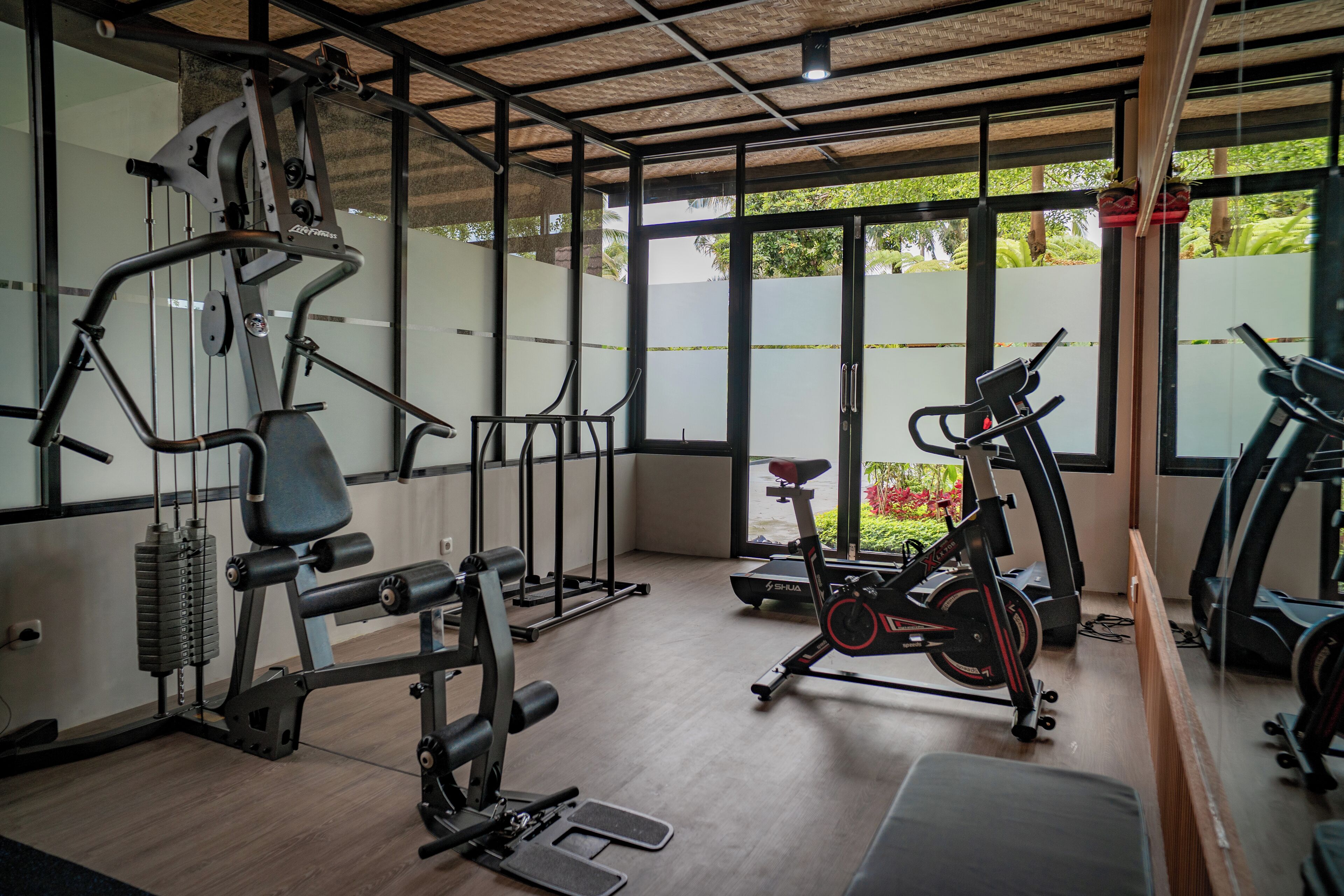 A gym with exercise equipment, large windows, and a view of greenery outside.