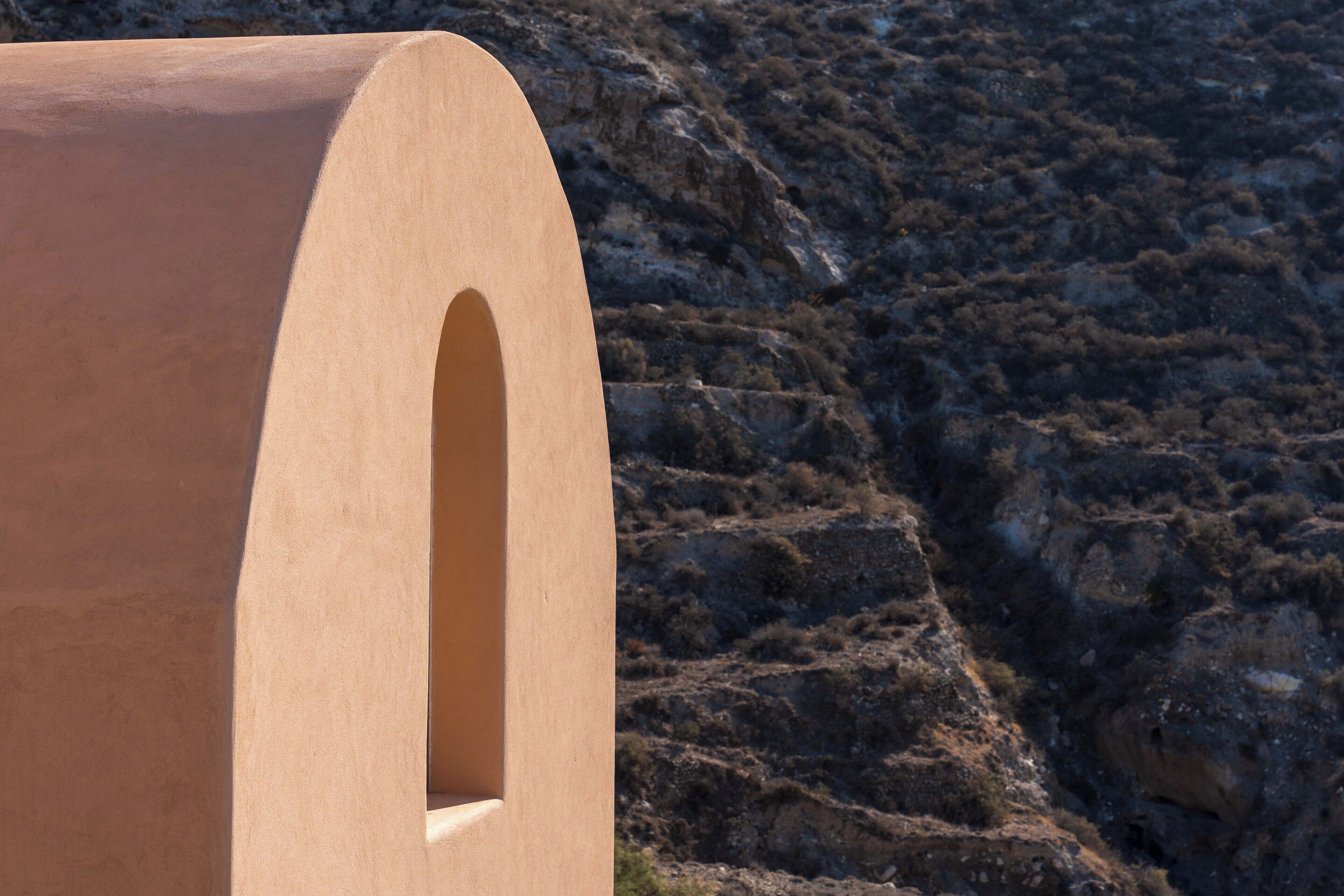 Una estructura de madera con diseño curvo y una abertura en arco, sobre un fondo de ladera rocosa.