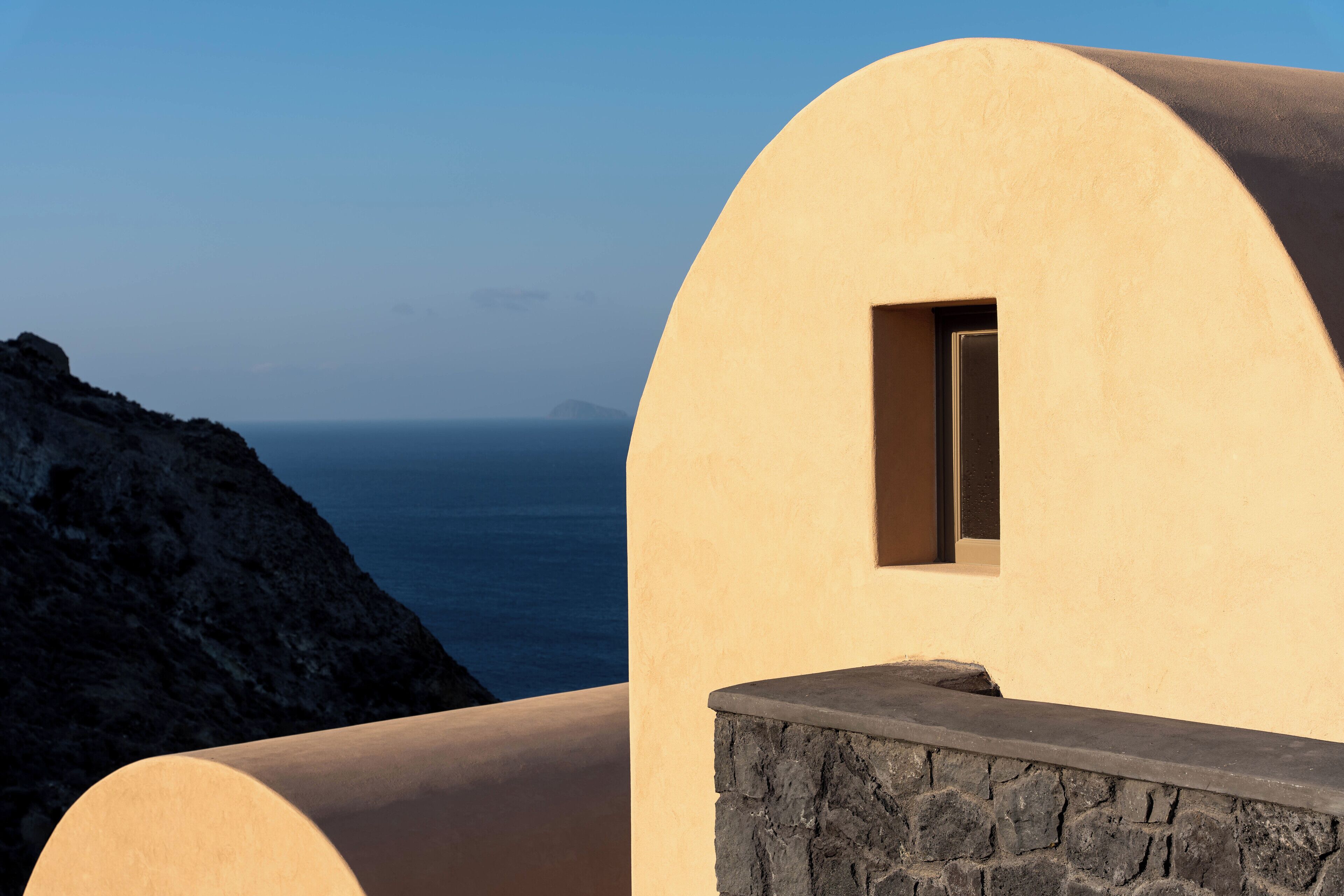Un edificio curvo con base de piedra y una ventana pequeña, con vistas a una costa rocosa y al mar.