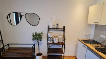 A compact kitchen with a wooden table, a shelf with kitchen appliances, and a wall-mounted mirror.