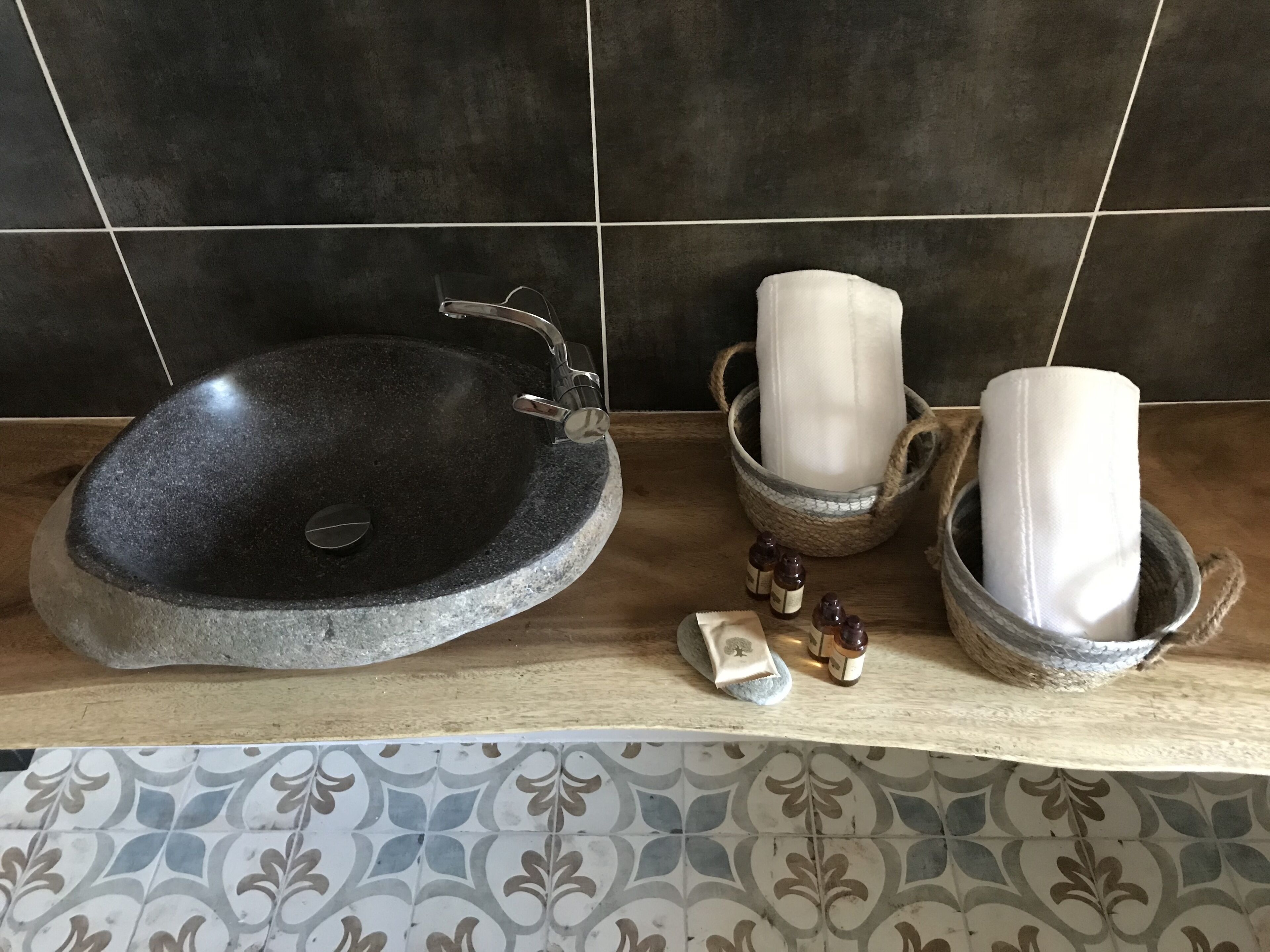 A bathroom with a stone sink, a towel holder with a rolled towel, and a small bottle of soap.