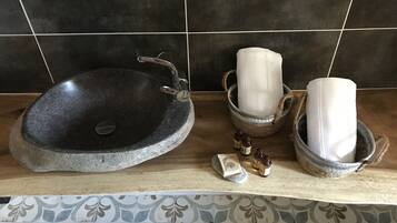 A bathroom with a stone sink, a towel holder with a rolled towel, and a small bottle of soap.