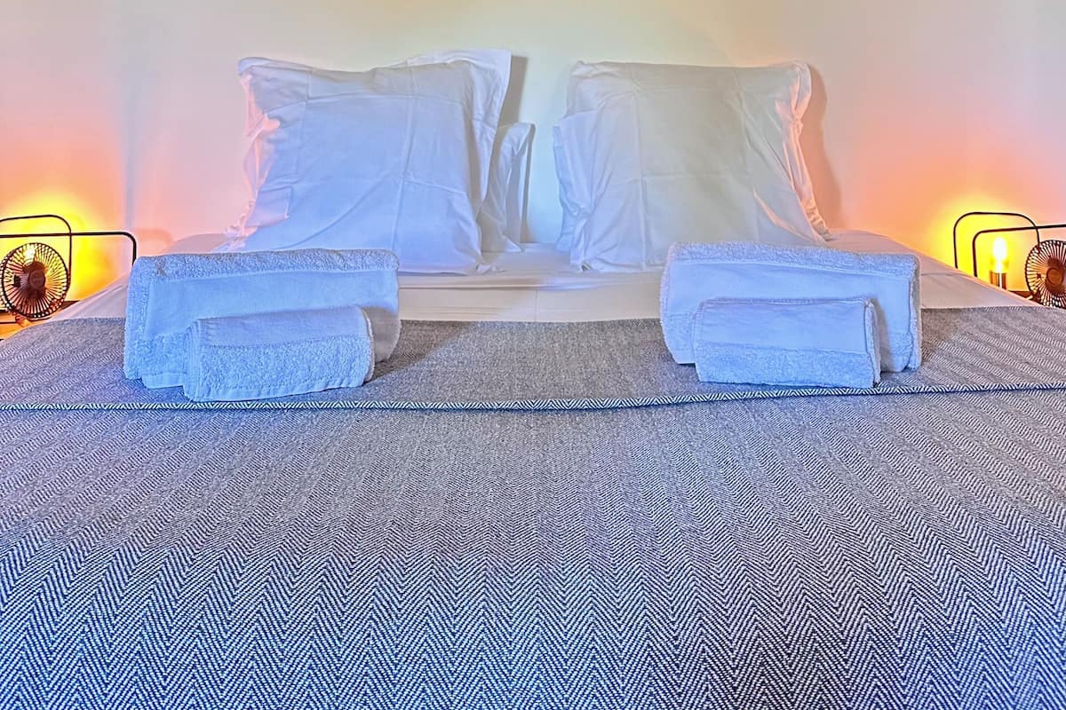 A bed with white linens, a patterned rug, and two wall-mounted lamps.