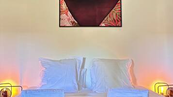 Una cama con ropa blanca, un tapete estampado y dos lámparas fijadas a la pared.