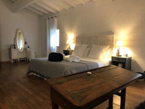 A hotel room with a bed, bedside tables with lamps, a wooden bench, a dressing table with a mirror, and a window with curtains. - Les Cailloux Dorés (Massillargues-Attuech)