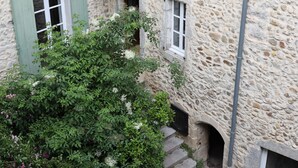 Un edificio de piedra con varias ventanas, algunas con contraventanas, y un pequeño jardín con abundante vegetación.