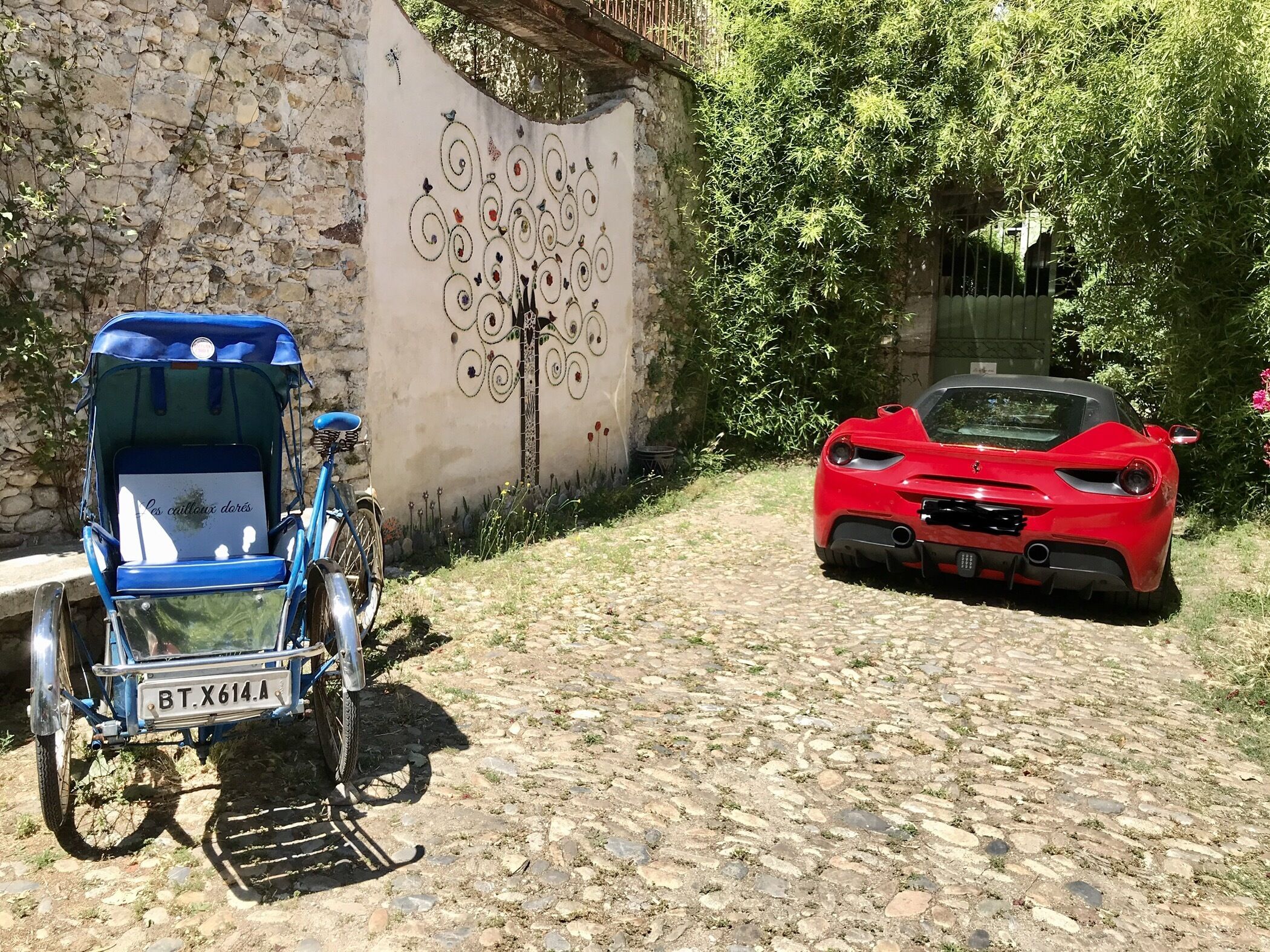 A cobblestone path with a blue rickshaw and a red sports car parked on the side.