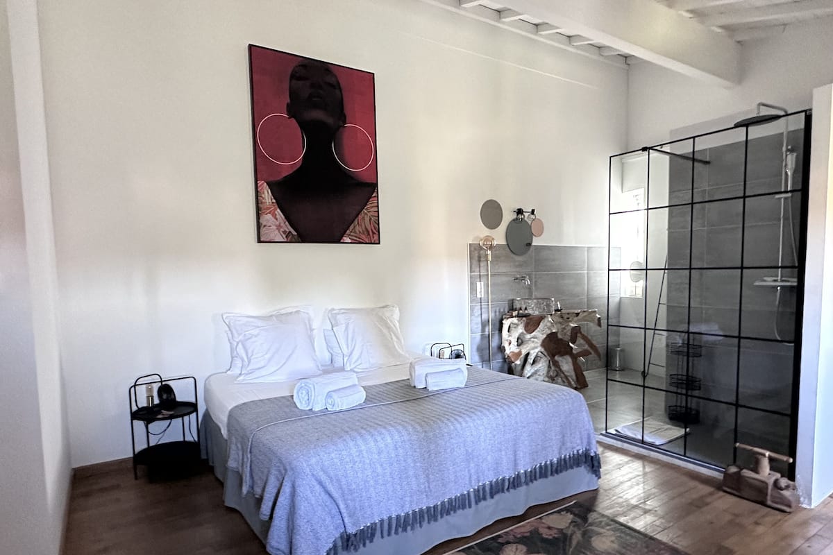 A modern bedroom with a large bed, a glass shower enclosure, and a mounted artwork.