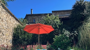 Una piscina con un paraguas rojo, paredes de piedra y un edificio de piedra al fondo.