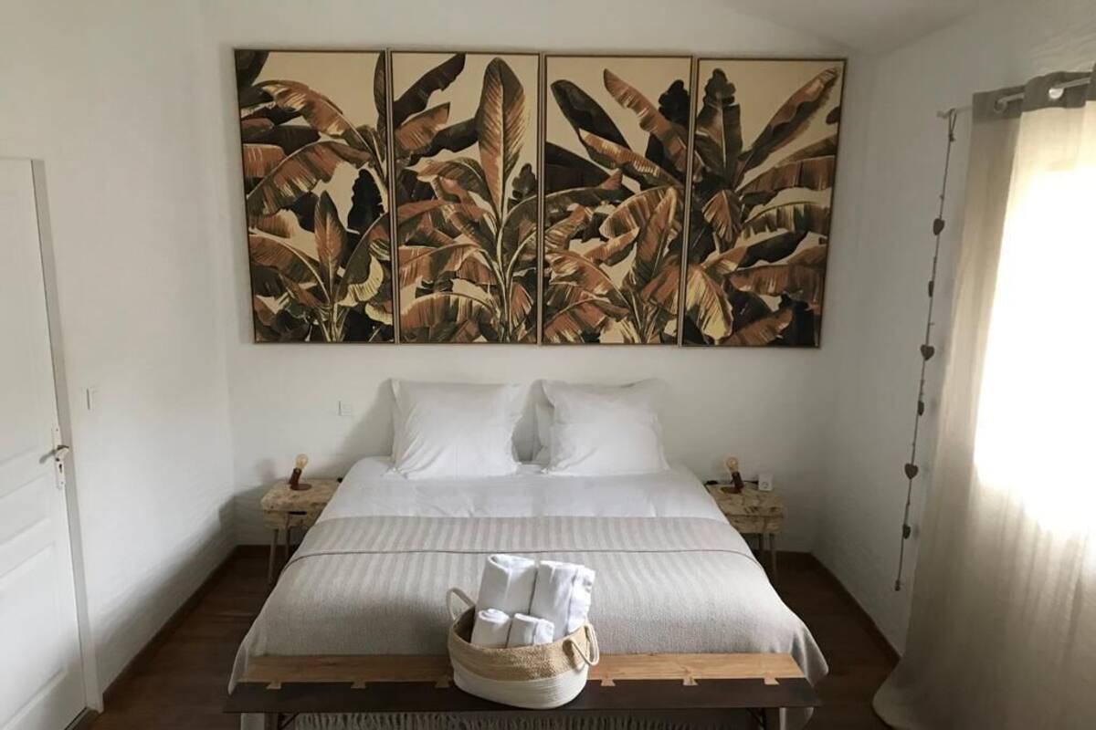 A neatly made bed with white linens, a bedside table with a lamp, and a wall-mounted artwork of large leaves.