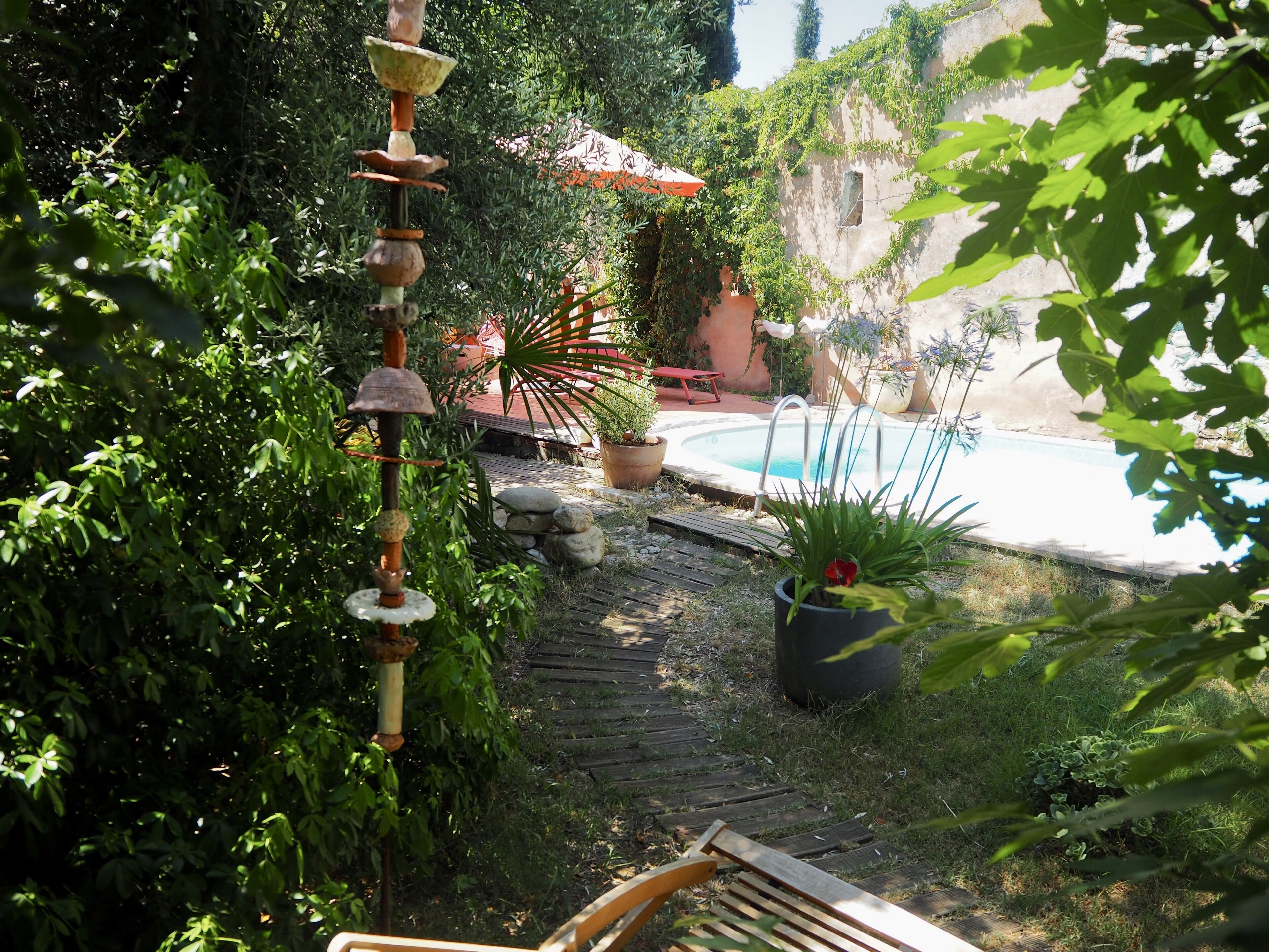 A garden with a wooden bench, a decorative wind chime, a pool, and potted plants.