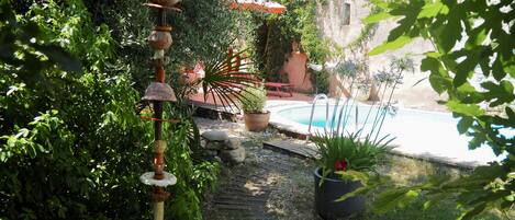 A garden with a wooden bench, a decorative wind chime, a pool, and potted plants.