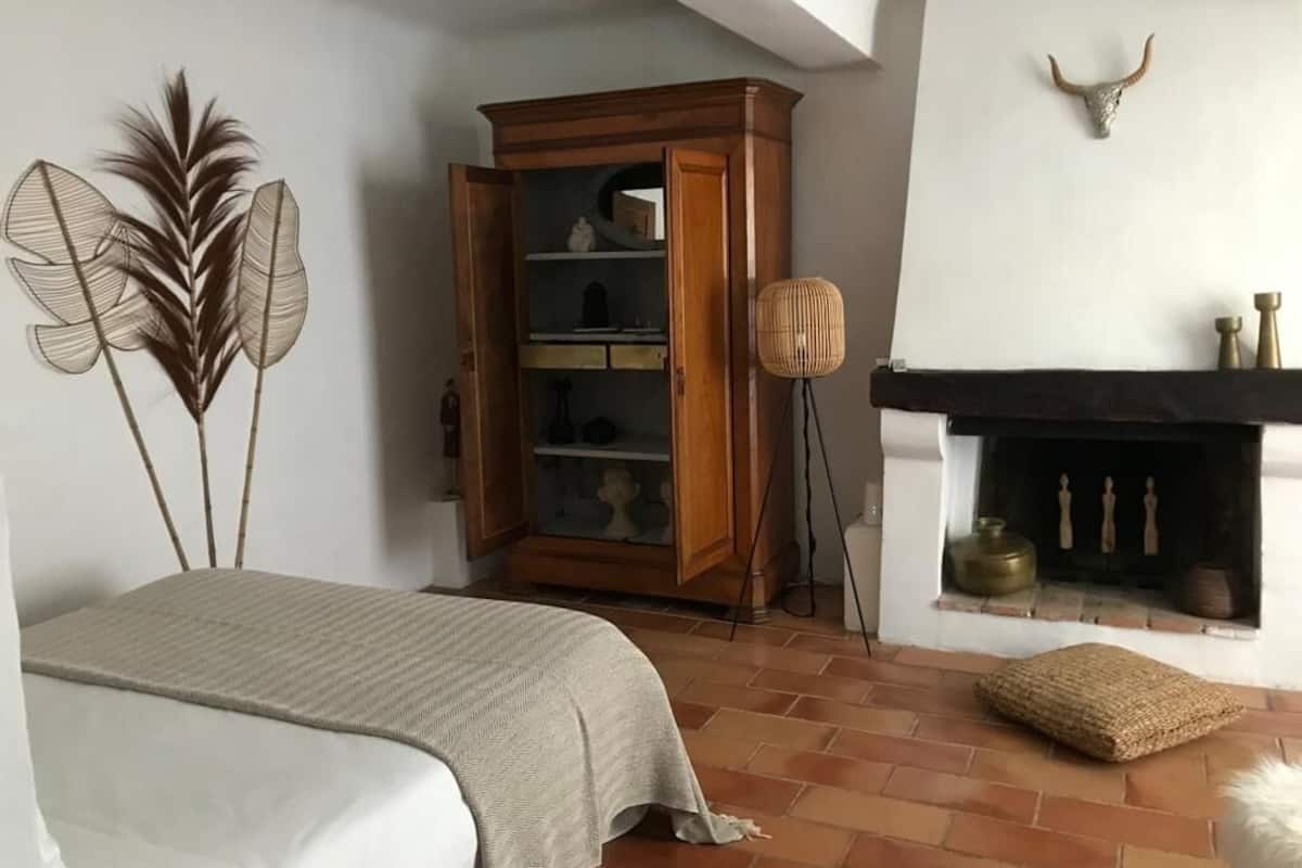 A bedroom with a bed, a wooden cabinet, a fireplace, and decorative wall art.