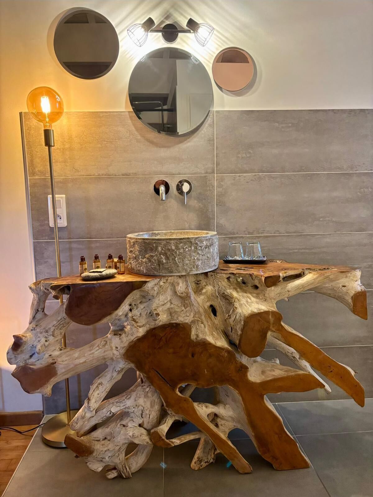 A bathroom with a unique wooden vanity, a round mirror, and a modern light fixture.