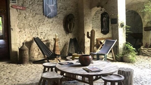 Un interior rústico de piedra con una mesa redonda de madera, sillas y lámparas colgantes.