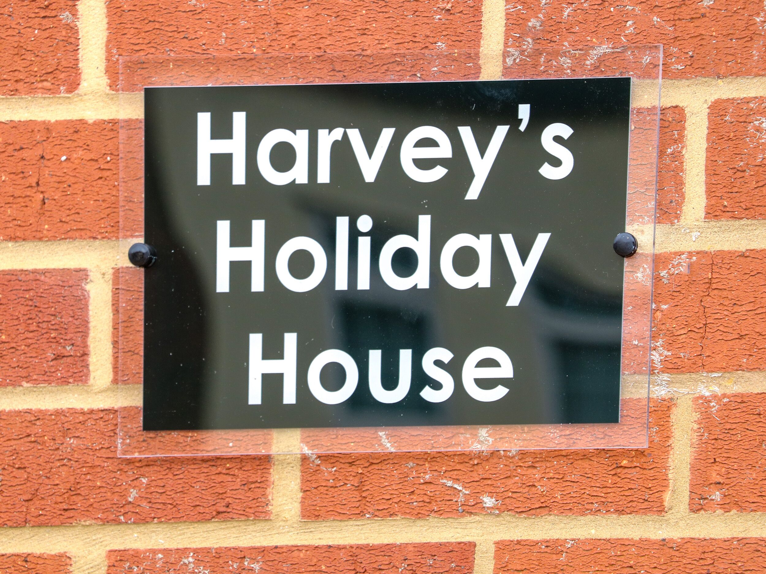 Een bord met de tekst 'Harvey's Holiday House' bevestigd aan een bakstenen muur.