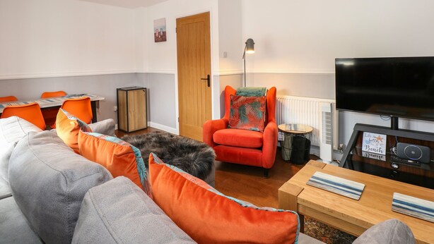 A living room with a sofa, armchairs, a TV, and a small table. - Harvey's Holiday House (Hunstanton)