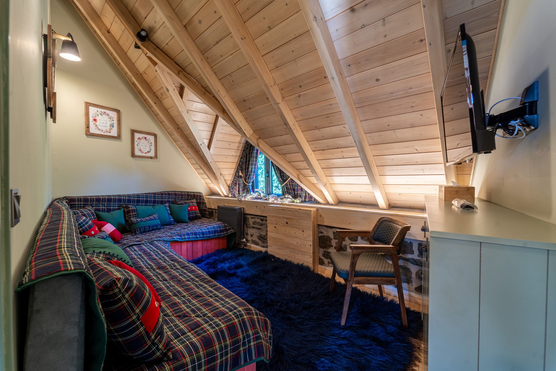 A cozy attic bedroom with a loft bed, a chair, a desk, and a television.