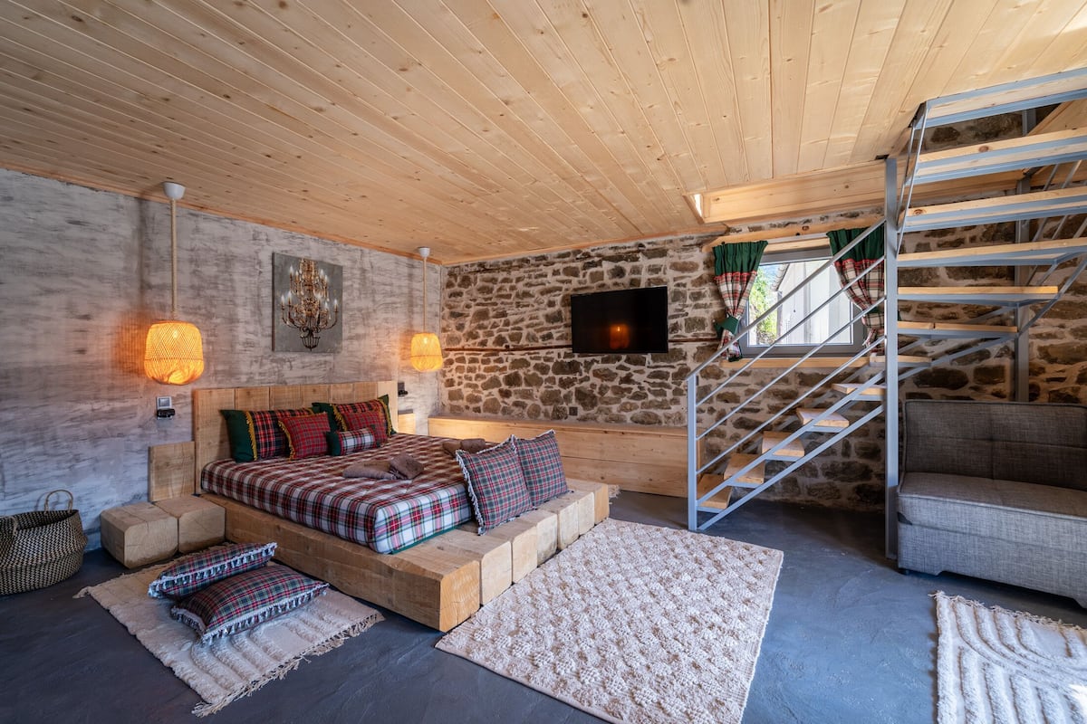 A cozy bedroom with a stone wall, a wooden bed, a TV, and a staircase.
