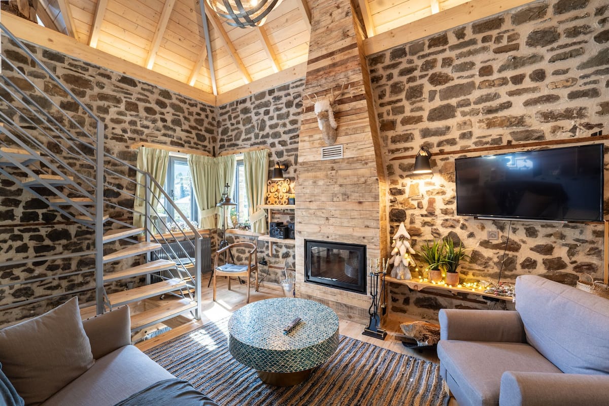 A cozy living room with a stone wall, a fireplace, a TV, and a staircase.